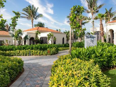 Hotel complex with Mediterranean-style buildings, palm trees, and well-maintained paths under a blue sky.