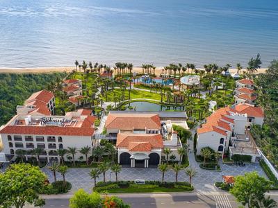 Aerial view of a resort with pool, green gardens, and ocean view in daylight.