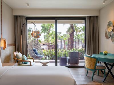 Modern hotel room with balcony, hanging chair, and tropical garden view.
