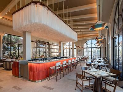 Modern restaurant with a long red bar, wooden tables, and large windows letting in natural light.