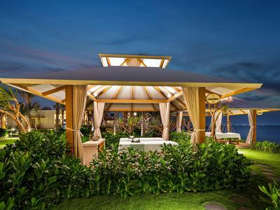 Illuminated beach pavilion with curtains and plants at dusk.
