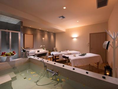 Spa moderno con camillas de masaje y una bañera grande con luz cálida.