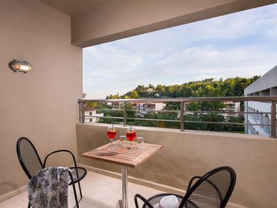 Balcón con mesa y sillas, vista a edificios y colinas bajo cielo parcialmente nublado.