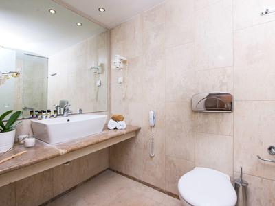 Baño moderno con inodoro blanco, lavabo, espejo y plantas en tonos neutros.