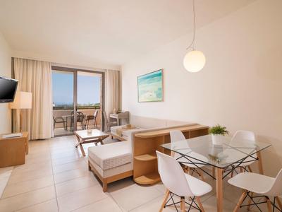Sala luminosa con sofá, zona de comedor, mesa de cristal y balcón con vistas en la habitación del hotel.