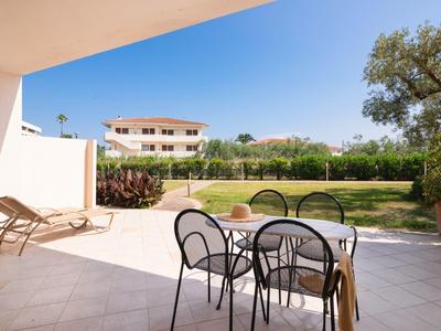 Terraza con mesa y sillas, vista a jardín cuidado y edificio bajo cielo despejado.