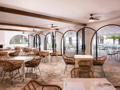 Helles, offenes Restaurant mit Korbstühlen und großen Bogenfenstern mit Blick nach draußen.