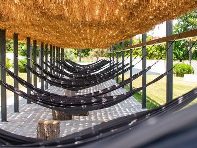 Mehrere schwarze Hängematten unter einem Strohdach neben einem Gartenweg.