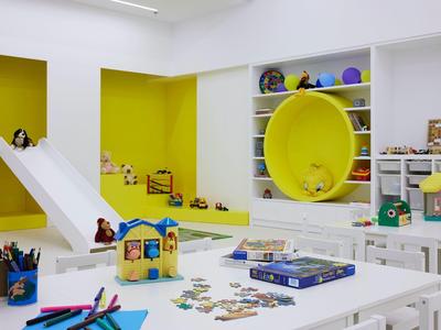Sala de juegos luminosa con tobogán, pared amarilla y varios juguetes para niños.