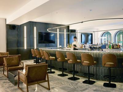 Bar de hotel moderna con sillones de cuero, barra y luz indirecta.