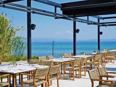 Offenes Restaurant mit Blick auf das blaue Meer und hellem Holzmobiliar unter einer Überdachung.