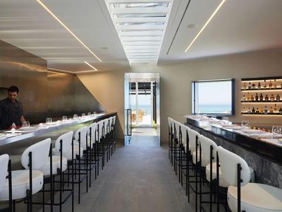 Modernes Restaurant mit langer Bar, weißen Stühlen und Barkeepern in elegantem Ambiente.