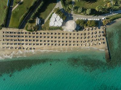 Vue aérienne d'une plage avec des rangées de parasols et de transats à côté d'une eau turquoise claire.