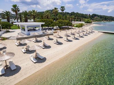 Hôtel de plage avec rangées de chaises longues et parasols le long d'une eau claire.
