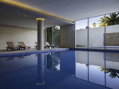 Piscine intérieure moderne avec chaises longues et grandes fenêtres vitrées donnant sur l'extérieur.