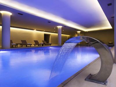 Piscine intérieure moderne avec cascade, chaises longues relaxantes et éclairage tamisé.