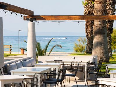 Espace repas ouvert avec tables, chaises et vue sur la mer, entouré de palmiers et de verdure.