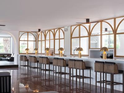 Espace bar d'hôtel moderne avec comptoir long et tabourets élégants sous de grandes fenêtres.