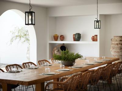 Salle à manger moderne avec grande table en bois, chaises en rotin et décoration minimaliste.