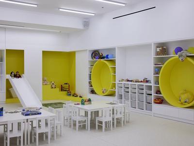 Salle de jeux lumineuse avec tables blanches, chaises et grands sièges ronds jaunes.