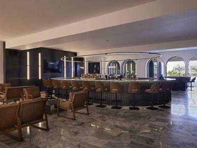 Salon d'hôtel moderne avec fauteuils en cuir, bar et grandes fenêtres donnant sur la terrasse.