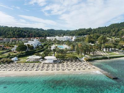 Complexe hôtelier avec piscine, palmiers et plage de sable au bord d'eau turquoise claire.