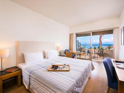 Chambre d'hôtel moderne avec lit double, bureau, chaise et balcon avec vue sur la mer.