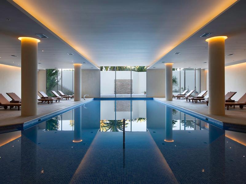 Piscina interior moderna con tumbonas y iluminación ambiental en un hotel.