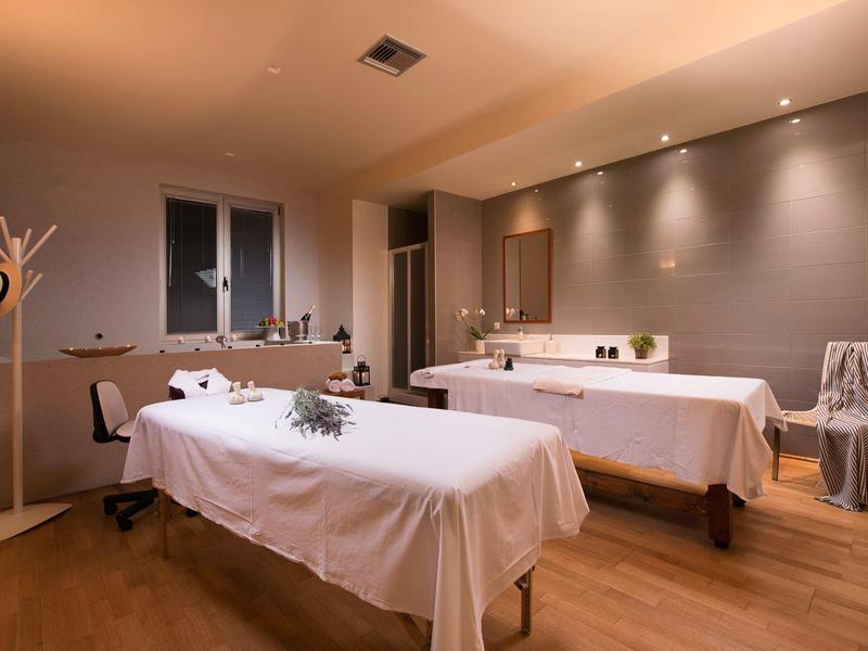 Una sala de masaje tranquila con dos camillas, iluminación suave y suelo de madera cálida.