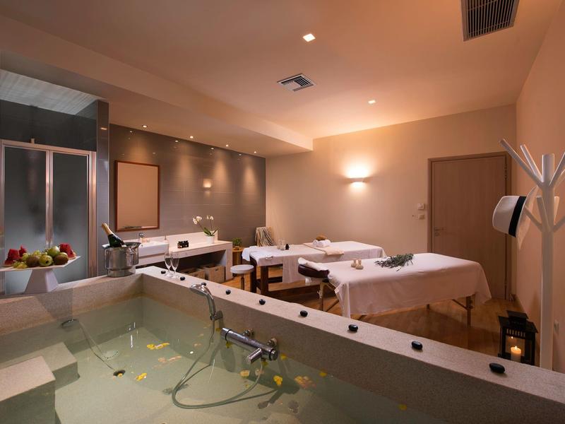 Spa moderno con camillas de masaje y una bañera grande con luz cálida.