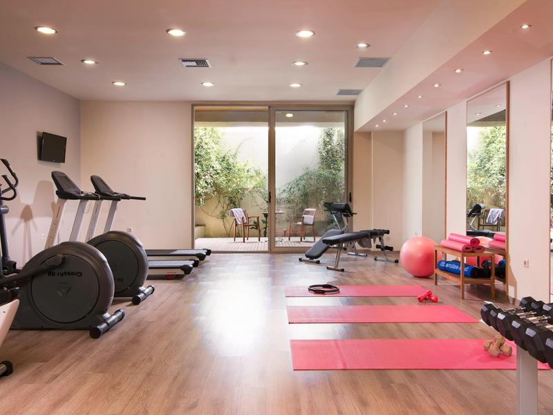 Gimnasio moderno con cintas de correr, pesas y esterillas frente a grandes ventanas.