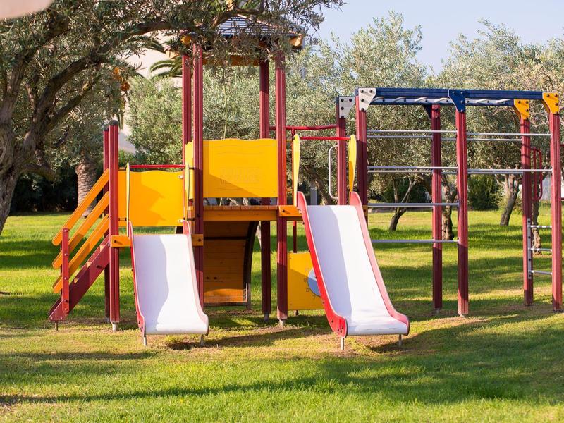 Parque infantil con dos toboganes blancos y estructura de escalada en un parque soleado.