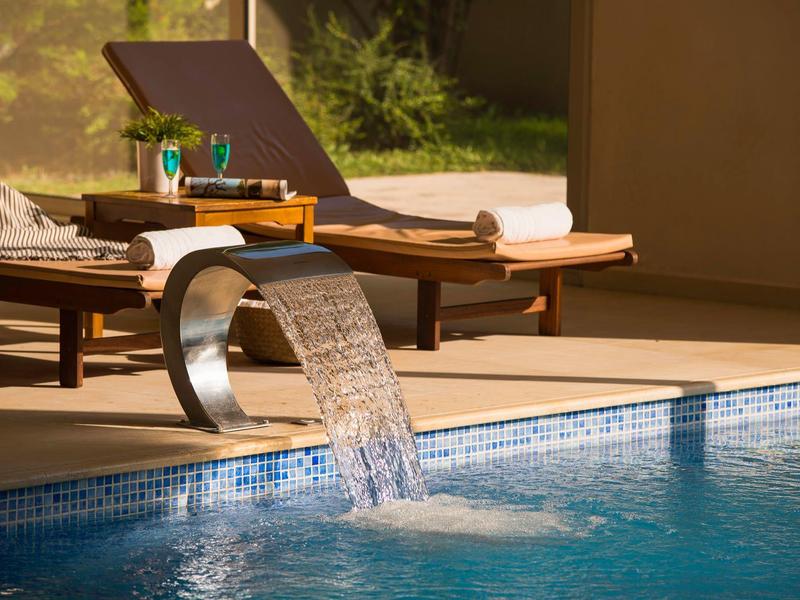 Vista de una piscina con una cascada metálica y tumbonas con toallas en un área de descanso