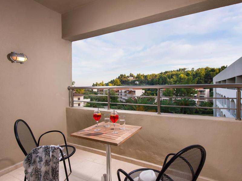 Balcón con mesa y sillas, vista a edificios y colinas bajo cielo parcialmente nublado.