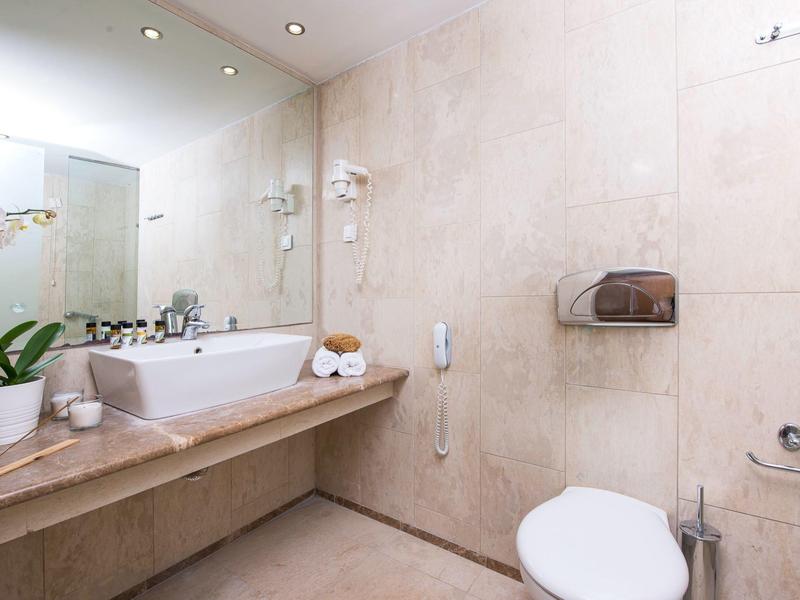 Baño moderno con inodoro blanco, lavabo, espejo y plantas en tonos neutros.