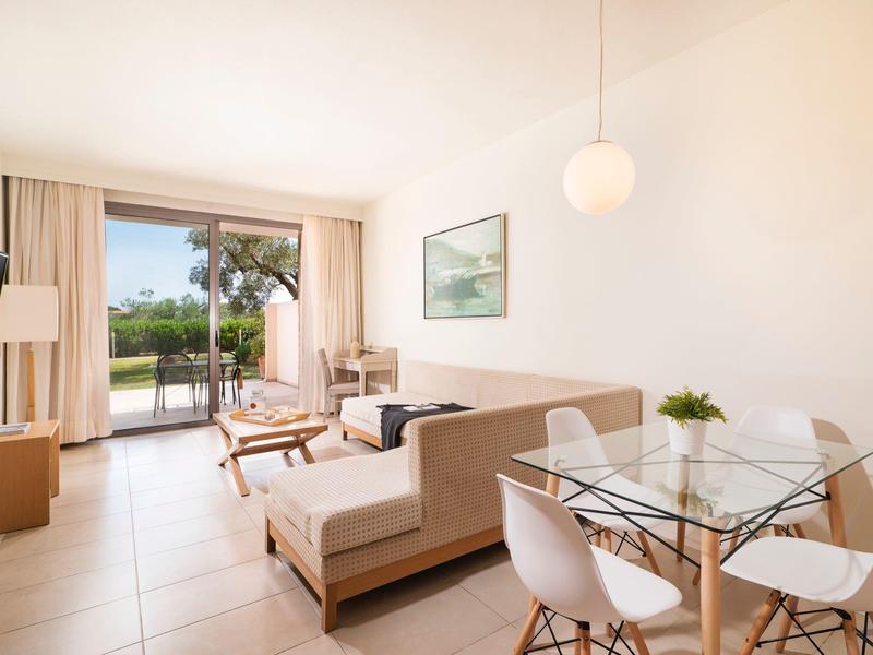 Sala luminosa con zona de comedor de cristal, sofá, televisor y acceso a terraza con vista al jardín.