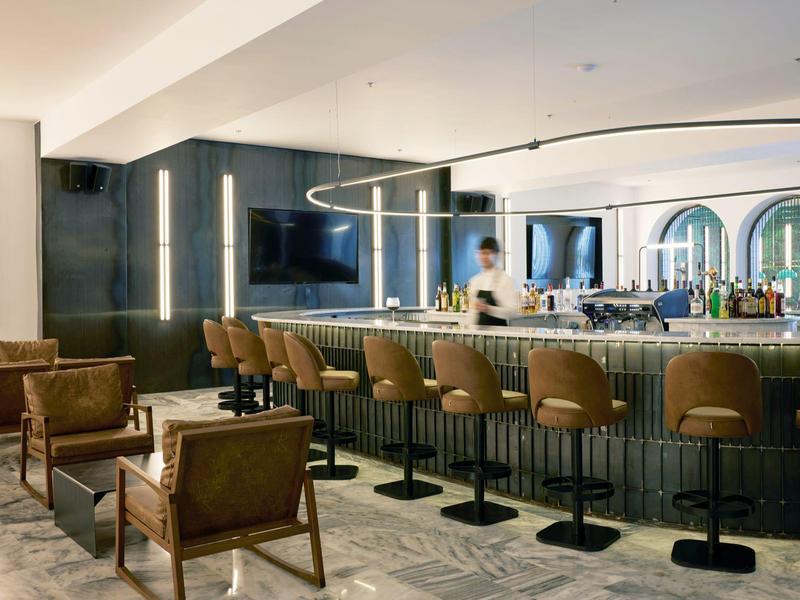 Bar de hotel moderna con sillones de cuero, barra y luz indirecta.