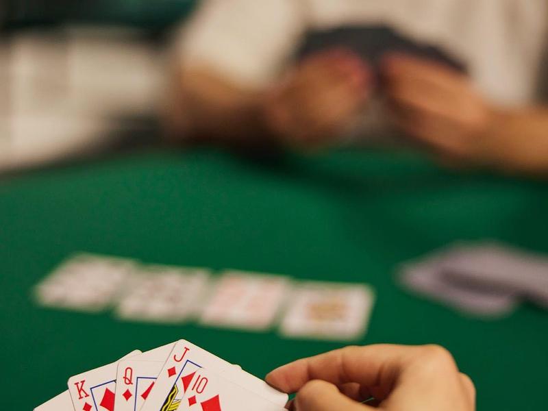 Personas jugando póker en una mesa de casino con cartas en la mano.