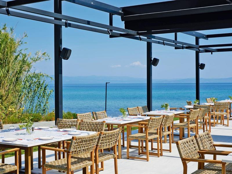 Restaurante al aire libre con muebles de ratán y vista al mar azul bajo un cielo despejado.