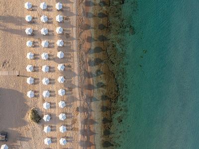Vista aérea de una playa con filas de sombrillas blancas y agua turquesa.