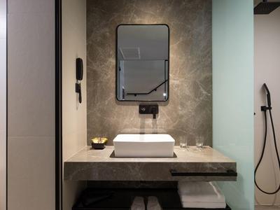 Lavabo moderno en cuarto de baño de hotel con espejo rectangular y fregadero sobre encimera gris de piedra.