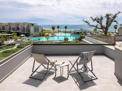 Blick auf einen Balkon mit zwei Liegestühlen, Tisch, Pool und Meer im Hintergrund.