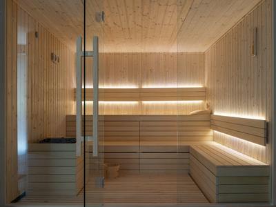 Sala de sauna de madera clara con iluminación indirecta y puerta de vidrio.