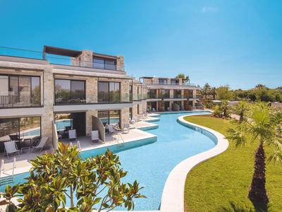 Moderner Hotelkomplex mit geschwungenem Pool und grüner Gartenanlage unter blauem Himmel.