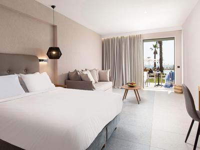 Habitación de hotel moderna con cama grande, zona de estar y vistas al balcón con vista al mar.