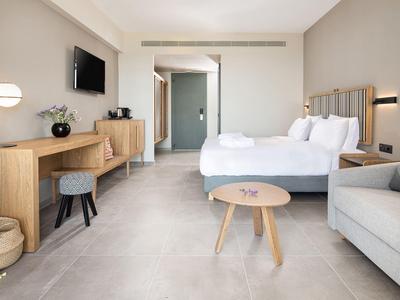 Habitación de hotel luminosa con dos camas, sofá, TV y mobiliario moderno de madera.