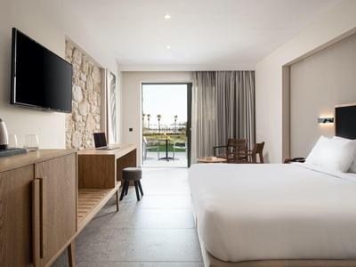 Habitación de hotel moderna con cama doble, televisor de pantalla plana y balcón con vista al exterior.