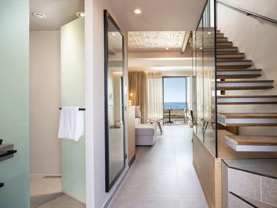 Corredor moderno de hotel con escalera de madera y vista al mar a través de grandes ventanas al fondo.