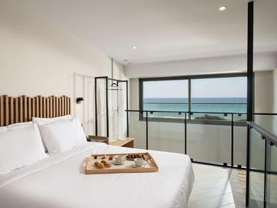 Habitación de hotel luminosa con cama doble y balcón con vista al mar.