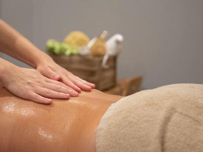 Manos masajeando la espalda aceitosa de una persona tumbada con una toalla beige.